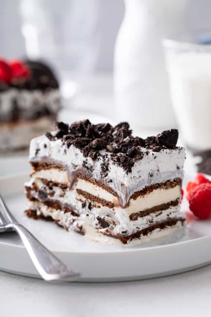 Close up view of a slice of ice cream sandwich cake next to a fork on a white plate.